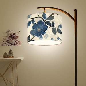 May include: A gold floor lamp with a white and blue floral patterned lampshade. The lampshade has a white inner lining and a gold trim.