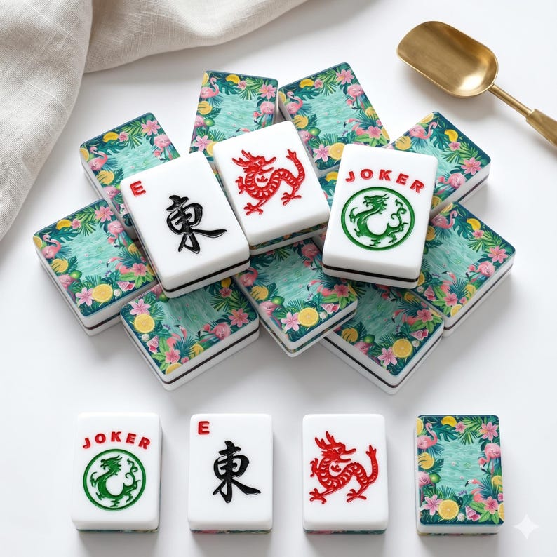 May include: A collection of white Mahjong tiles with black, red, and green symbols. The tiles are decorated with a tropical floral design. A gold spoon rests in the background.