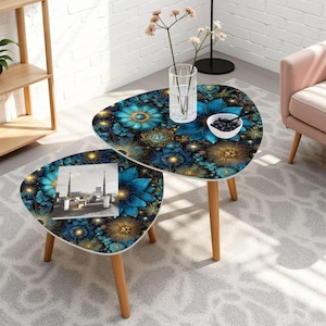 May include: Two nesting side tables with a floral design. The tables have a dark background with blue and gold flowers. The tables have light wood legs and a triangular shape. One table has a photo on it.
