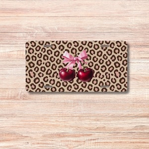 May include: A brown and pink leopard print license plate with two red cherries tied together with a pink bow.