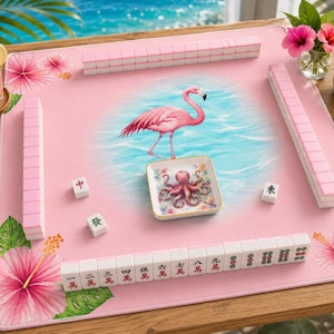 May include: A square pink mahjong mat featuring a central illustration of a pink flamingo standing in blue water. The mat is decorated with hibiscus flowers and lemon slices. A small square dish with an octopus graphic and mahjong tiles are placed on the surface.