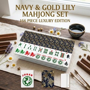 K&ouml;nnte beinhalten: Ein Navy & Gold Lily Mahjong-Set, 166-teilige Luxusausgabe. Das Set enth&auml;lt wei&szlig;e Spielsteine mit gr&uuml;nen und roten Symbolen, eine marineblaue und goldfarbene H&uuml;lle mit floralem Muster und eine kleine Tasse. Der Text auf der Box lautet "Navy & Gold Lily Mahjong Set 166 Piece Luxury Edition."