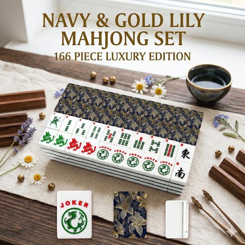 K&ouml;nnte beinhalten: Ein Navy & Gold Lily Mahjong-Set, 166-teilige Luxusausgabe. Das Set enth&auml;lt wei&szlig;e Spielsteine mit gr&uuml;nen und roten Symbolen, eine marineblaue und goldfarbene H&uuml;lle mit floralem Muster und eine kleine Tasse. Der Text auf der Box lautet "Navy & Gold Lily Mahjong Set 166 Piece Luxury Edition."