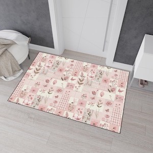 May include: A rectangular doormat with a patchwork design featuring floral and leaf patterns in shades of pink, beige, and brown. The mat has a black border and is placed in front of a white door.