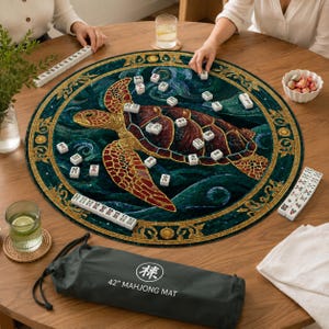 K&ouml;nnte beinhalten: Eine runde 107 cm gro&szlig;e Mahjong-Matte mit einer Meeresschildkr&ouml;ten-Illustration in Rot-, Gold- und Petrolt&ouml;nen sowie einem dekorativen Rand. Dazu geh&ouml;ren eine schwarze Aufbewahrungstasche mit der Aufschrift 42" MAHJONG MAT, Spielsteine und S&uuml;&szlig;igkeiten.