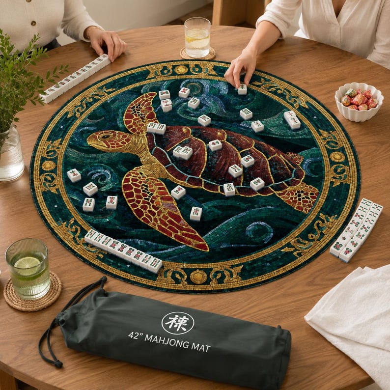 K&ouml;nnte beinhalten: Eine runde 107 cm gro&szlig;e Mahjong-Matte mit einer Meeresschildkr&ouml;ten-Illustration in Rot-, Gold- und Petrolt&ouml;nen sowie einem dekorativen Rand. Dazu geh&ouml;ren eine schwarze Aufbewahrungstasche mit der Aufschrift 42" MAHJONG MAT, Spielsteine und S&uuml;&szlig;igkeiten.