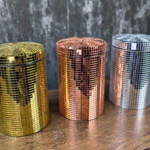 以下が含まれることがあります： モザイクタイルのデザインが施された装飾的な容器が3つあります。容器は金色、ローズゴールド、銀色です。