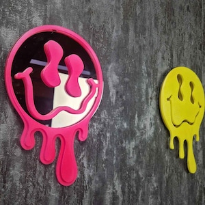 May include: Two wall-mounted smiley face mirrors, one pink and one yellow, with dripping edges. The pink mirror is a reflective surface with a smiley face design.