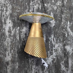 Könnte beinhalten: Eine goldene und silberne Hängelampe in Form eines UFOs mit einer Kuhfigur, die unten hängt.