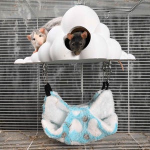 May include: A white cloud-shaped pet house with two openings, suspended above a blue and white patterned hammock. Two small rats are visible, one inside the cloud and one on top. The cage has a wire frame.