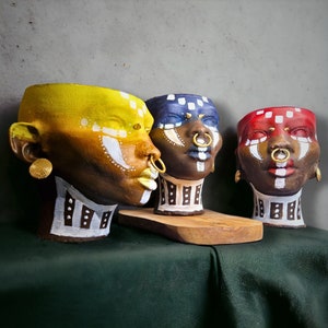 Peut inclure: Trois pots en céramique avec des visages peints et des anneaux de nez en or. Les pots sont jaune, bleu et rouge avec des détails blancs et noirs.