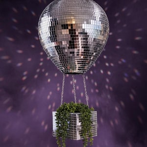 May include: A mirrored disco ball planter with a square, mirrored planter box suspended below. The planter box is filled with green, trailing plants. The background is a dark purple with light reflections.