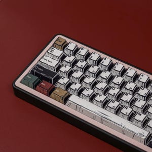 May include: A custom mechanical keyboard with white keycaps featuring black line art and Korean characters. The keyboard has a black frame with a pink border and colorful accent keys. The background is a deep red.