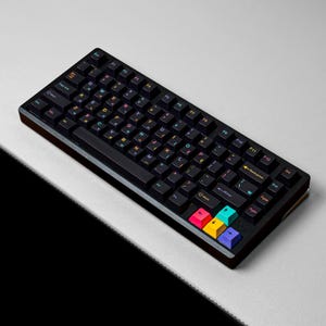May include: A black mechanical keyboard featuring dark keycaps with multicolored letters and symbols. The arrow keys are highlighted in bright pink, yellow, teal, and purple. The layout includes a standard function row and a dedicated backspace key.