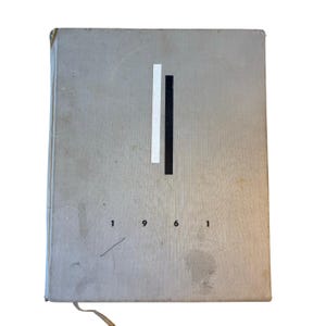 Könnte beinhalten: Ein graues Buch mit einem schwarz-weißen Design auf dem Einband. Das Jahr 1961 ist auf dem Einband gedruckt.