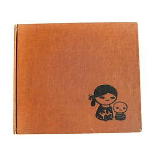Puede incluir: Un libro cuadrado de color marrón anaranjado con una ilustración negra de una mujer y un niño. La ilustración está en la esquina inferior derecha del libro. El libro tiene una superficie texturizada.
