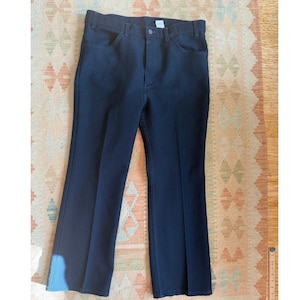 Puede incluir: Pantalones azul marino oscuro con un diseño clásico de cinco bolsillos. Los pantalones tienen un corte de pierna recta y un cierre de botón y cremallera. La tela parece ser un material resistente y duradero, adecuado para el uso diario. Los pantalones están planos sobre una alfombra estampada.