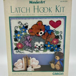 Könnte beinhalten: Ein WonderArt-Häkelset mit einem Design mit einem Teddybären, einem grauen Welpen und einem roten Herzen. Das Set enthält den Text "Baby Morning Light" und misst ca. 60,9 cm x 86,3 cm.