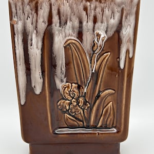 May include: A brown ceramic planter with white glaze dripping down the sides. The planter has a raised design of a flower with leaves.