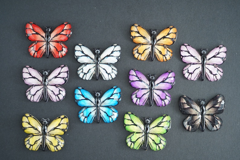 May include: Assortment of 10 colorful butterfly embellishments with black outlines. The butterflies are made of plastic and have a glossy finish. They are perfect for adding a touch of whimsy to crafts, scrapbooking, and other projects.