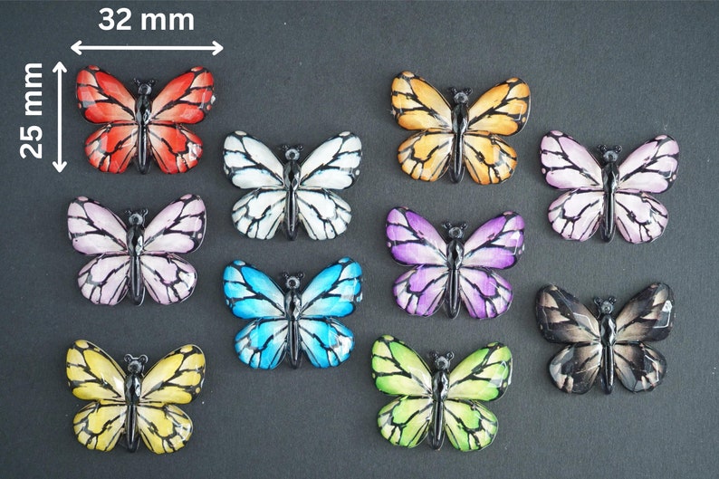 May include: Ten colorful butterfly embellishments, each measuring approximately 1 inch in diameter. The butterflies are made of plastic and have a glossy finish. The colors include red, white, yellow, blue, purple, and black.