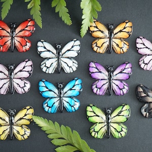May include: Ten colorful butterfly-shaped resin embellishments with black outlines. The butterflies are in various colors, including red, pink, white, blue, purple, yellow, and green.