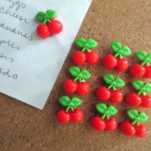 May include: A corkboard with a handwritten grocery list and 12 red and green cherry push pins.