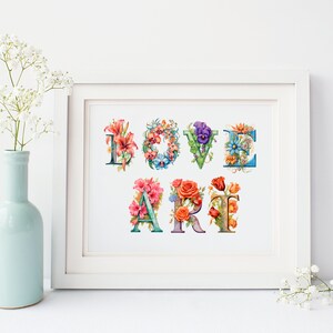 以下が含まれることがあります： 花で飾られたカラフルな文字で「LOVE ART」と書かれた白い額縁のプリント。文字はビンテージスタイルのフォントです。