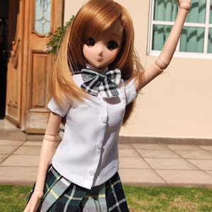 May include: A doll wearing a white collared shirt with a green and black plaid bow tie and a green and black plaid skirt. The doll is standing in front of a house with a wooden door and a window.