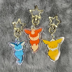 May include: Three iridescent keychains featuring cartoon versions of the Pokemon Eevee evolutions: Vaporeon, Flareon, and Jolteon. Each keychain is attached to a gold star-shaped swivel clasp.