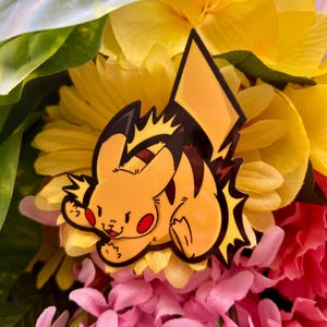 Puede incluir: Una pegatina de personaje de dibujos animados amarillo y negro de Pikachu, un personaje popular de Pokemon, con un diseño de rayo. La pegatina está sobre un fondo de flores amarillas y rosas.