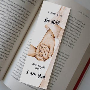Könnte beinhalten: Ein Lesezeichen mit einer Aquarell-Illustration von zwei Händen, die sich halten. Der Text "Sei still und wisse, dass ich Gott bin" steht auf dem Lesezeichen, zusammen mit dem Bibelvers "Psalm 46:10".