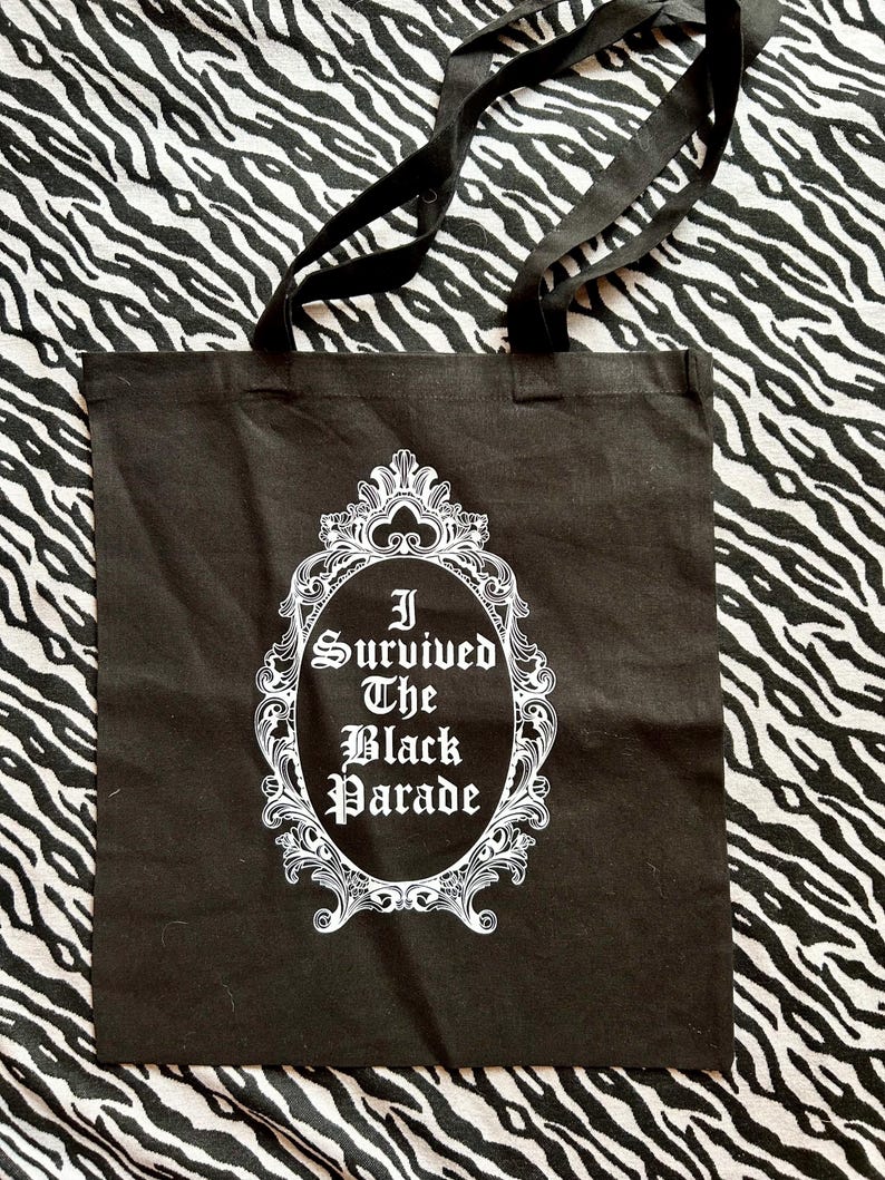 May include: Black canvas tote bag with white text and a decorative frame. The text reads "I Survived The Black Parade".