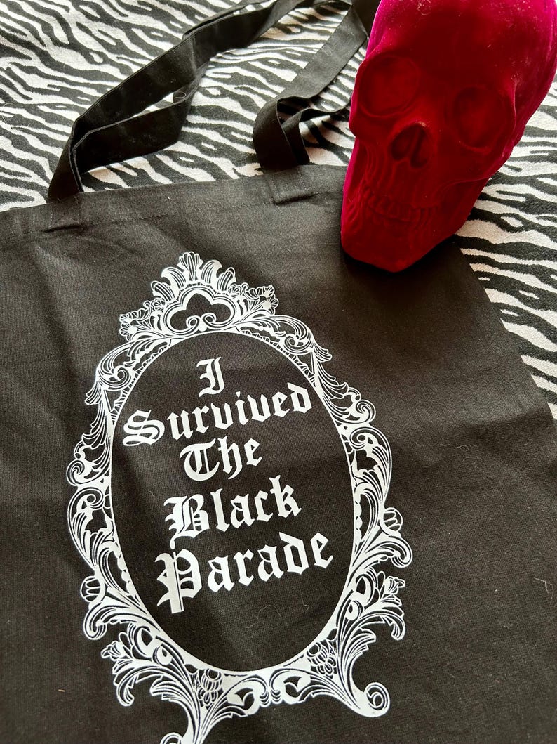 May include: Black canvas tote bag with a white ornate frame and the text "I Survived The Black Parade" inside.