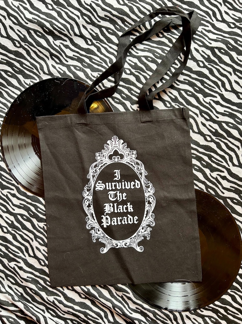 May include: Black tote bag with white text and a decorative frame. The text reads "I Survived The Black Parade".