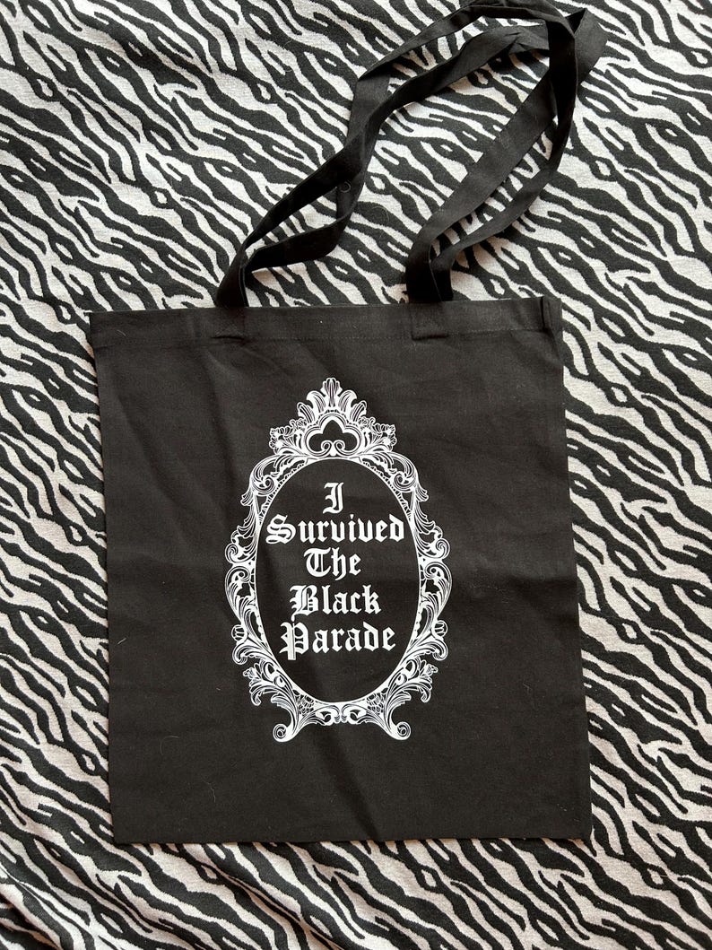 May include: Black tote bag with white text that reads "I Survived The Black Parade" inside a decorative white frame.