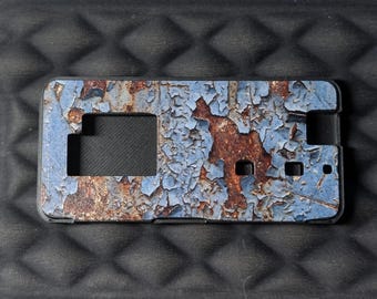 May include: A rectangular phone case featuring a weathered, distressed finish with a pattern of peeling light blue paint revealing a dark, textured rust-coloured surface underneath. The case includes precise cutouts for a camera and buttons.