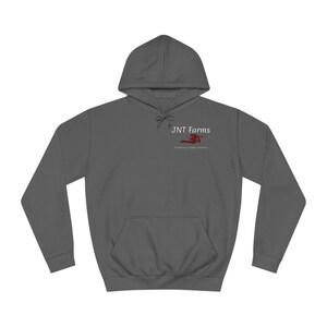 Könnte beinhalten: Ein anthrazitfarbener Kapuzenpullover mit einer Vordertasche und einer Kapuze mit Kordelzug. Auf der oberen linken Brust befindet sich der Text "JNT Farms" über einer roten Grafik eines Mähdreschers. Darunter steht der Satz "Cultivating a Family Tradition."