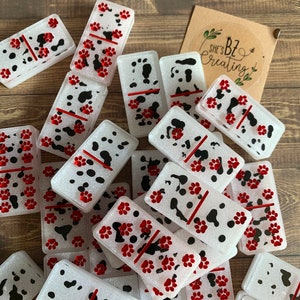 May include: A set of white dominoes with red paw prints and black spots. The dominoes are arranged in a pile on a wooden surface. The text "She's Bz Creating" is visible on a brown tag.