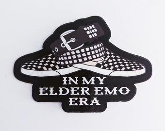 Puede incluir: Una pegatina en blanco y negro con un par de zapatillas a cuadros con un cinturón negro. El texto "IN MY ELDER EMO ERA" se muestra en letras blancas sobre un fondo negro.