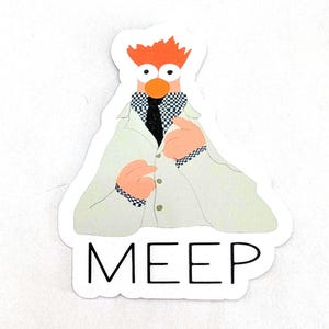 May include: A sticker featuring a cartoon character with orange hair, an orange nose, and large eyes. The character wears a white lab coat, a black tie, and a checkered collar. The word "MEEP" is printed in black block letters at the bottom.