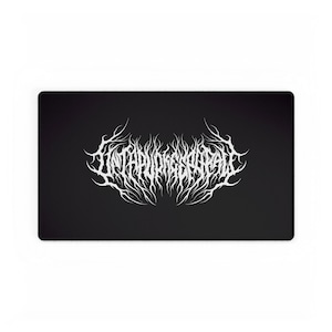 May include: A black rectangular desk mat featuring white, stylized text that reads "INTAPURIGSCARALE" in a gothic font. The text is centered and surrounded by flame-like designs, creating a bold, eye-catching design. This desk mat is ideal for adding a unique touch to any workspace.