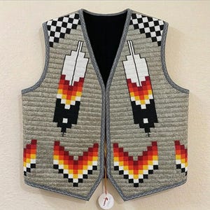 May include: A beaded vest with a gray background and a black interior. The vest features feather and geometric designs in red, yellow, black, and white. The edges are trimmed with gray and the top corners have a black and white checkered pattern.