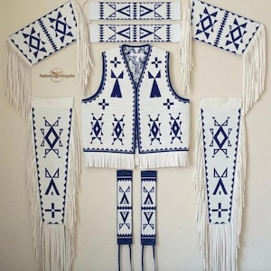 Può includere: Un gilet bianco con motivi geometrici blu scuro e frange, accompagnato da bracciali, fasce per le gambe e pannelli rettangolari abbinati, tutti caratterizzati da motivi tribali blu e bianchi e lunghe frange bianche.