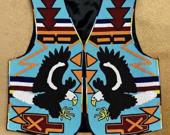 Puede incluir: Un chaleco sin mangas con intrincados abalorios sobre un fondo azul claro. El diseño incluye dos águilas negras con cabezas blancas y picos amarillos, acentuadas por patrones geométricos en granate, naranja, blanco y negro. El chaleco tiene un forro negro.