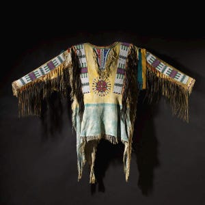 May include: A Native American-style tunic with long sleeves and fringed edges. The garment features a yellow body with a sunburst design, beaded accents, and colorful geometric patterns. The sleeves are adorned with white and purple beadwork.