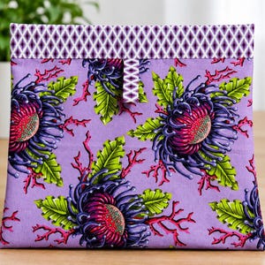 May include: A rectangular fabric pouch featuring a light purple background with a repeating pattern of dark purple and magenta spiky flowers, bright green leaves, and coral-like branches. The top edge has a purple and white diamond pattern.