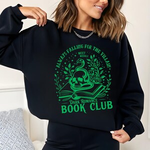 May include: Black sweatshirt with a green graphic design. The design features a skull, snake, and floral elements, with the text "ALWAYS FALLING FOR THE VILLAIN" and "DARK ROMANCE BOOK CLUB".