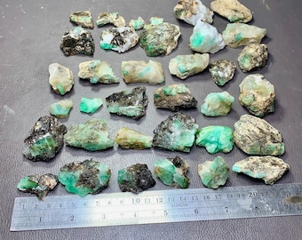 Op de afbeelding: Een verzameling ruwe smaragd kristallen in verschillende maten en vormen. De kristallen zijn een levendige groene kleur en hebben een natuurlijke, ongepolijste uitstraling.
