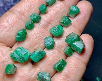 Op de afbeelding: Een verzameling kleine, groene smaragd kristallen. De kristallen zijn gefacetteerd en hebben verschillende vormen en maten.
